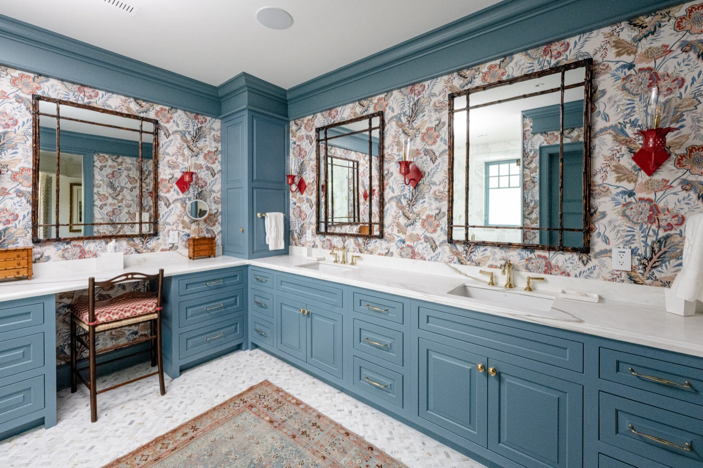 Custom blue double bath vanity cabinetry with brass hardware and floral wallpaper